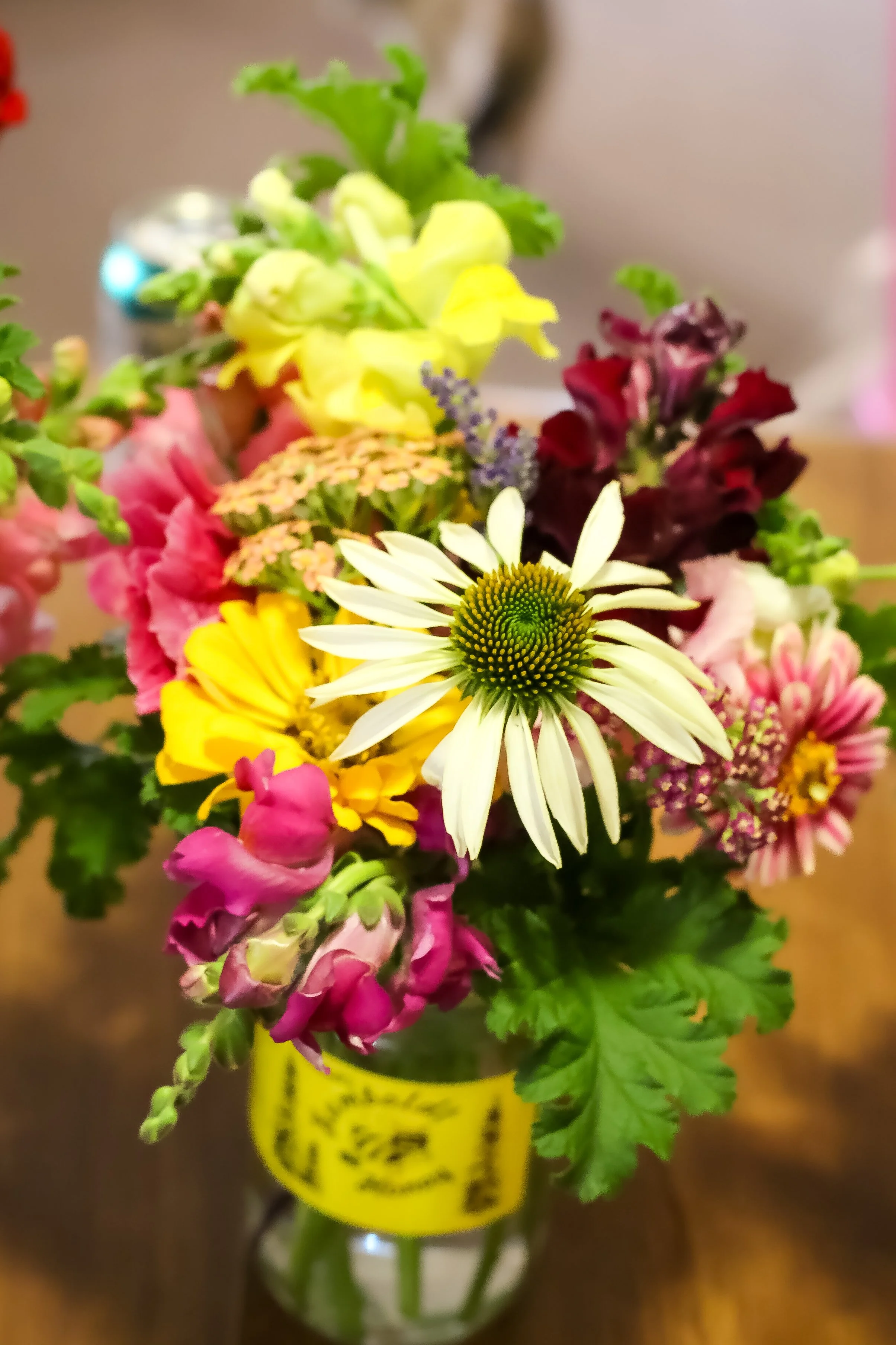 Colorful bouquet of various flowers in a small glass vase on a wooden surface.