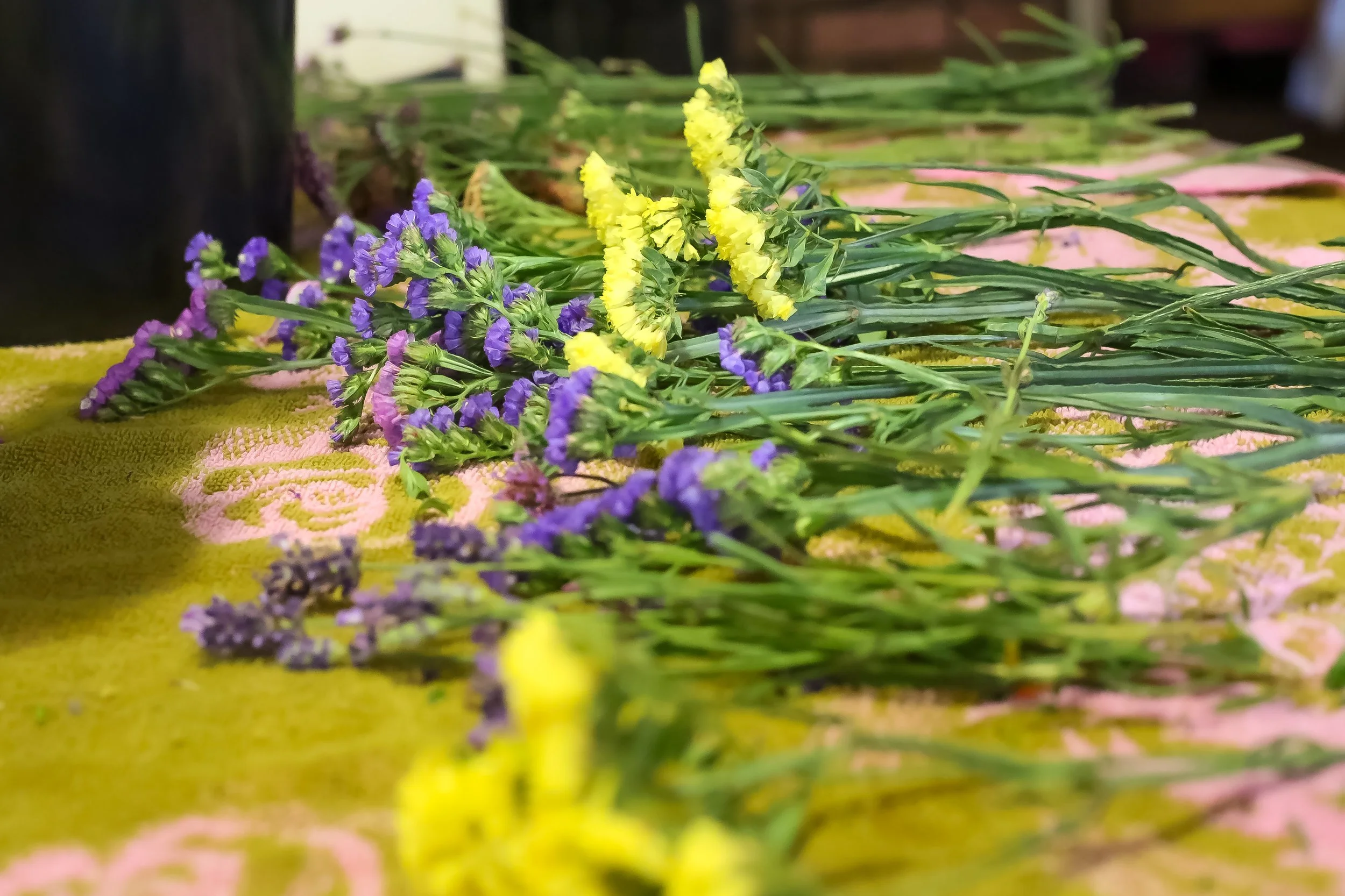 Various small yellow and purple flowers with green stems laid on a pink and yellow patterned cloth.