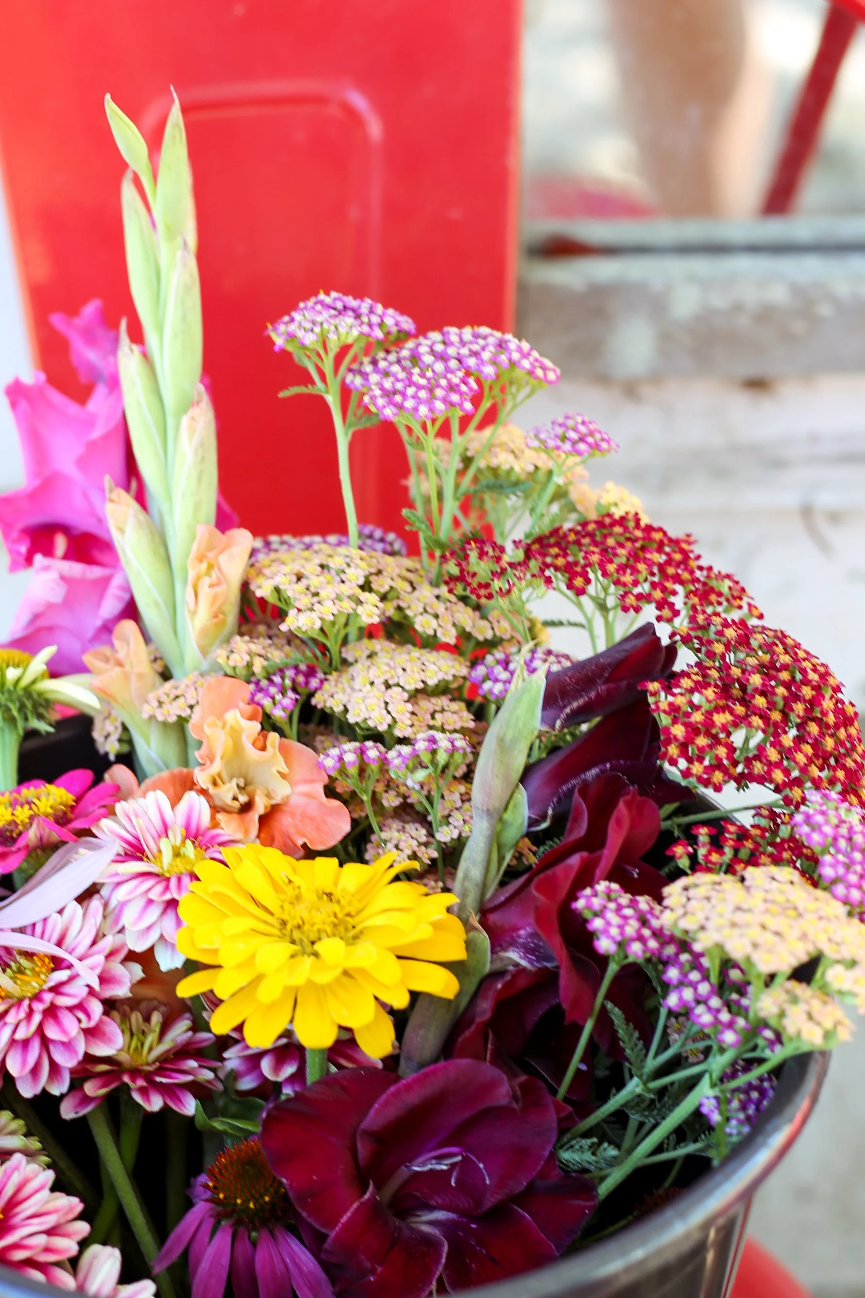 A colorful assortment of flowers in a bucket, including yellow, pink, purple, and deep red blooms.