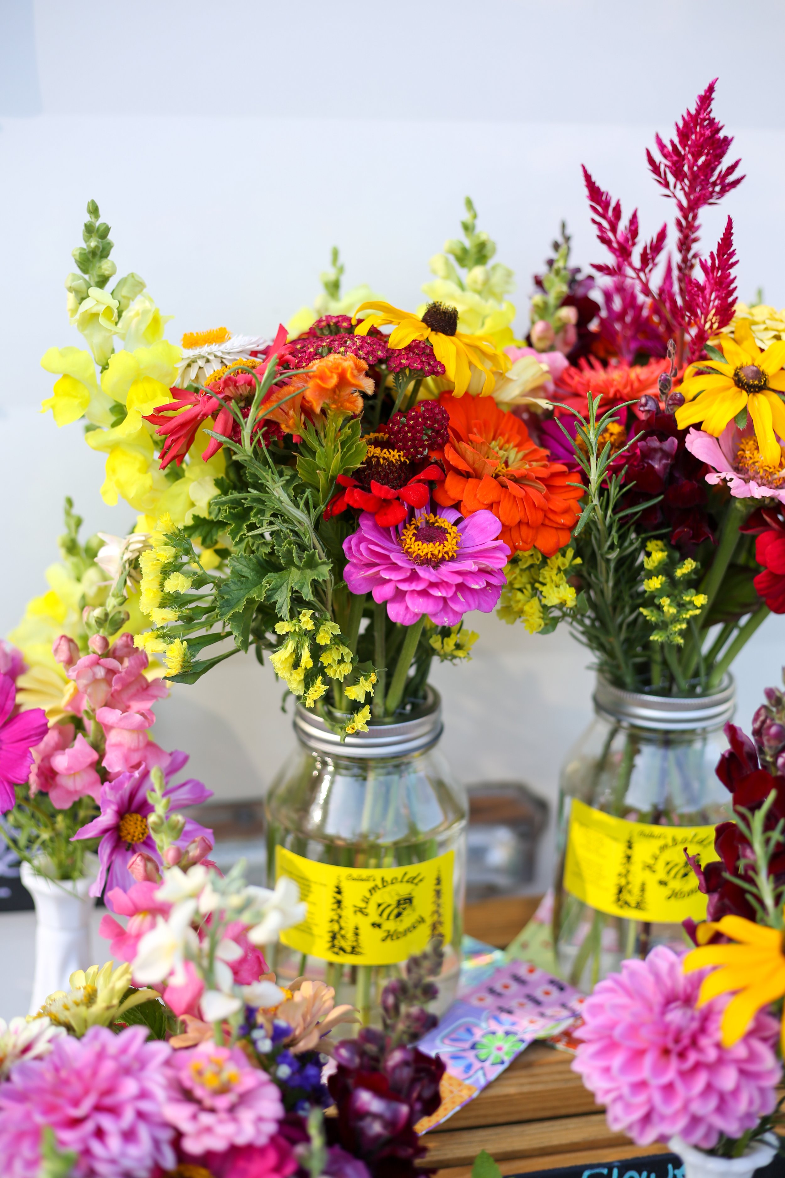 Colorful flower arrangements in glass jars with yellow labels on a wooden table.