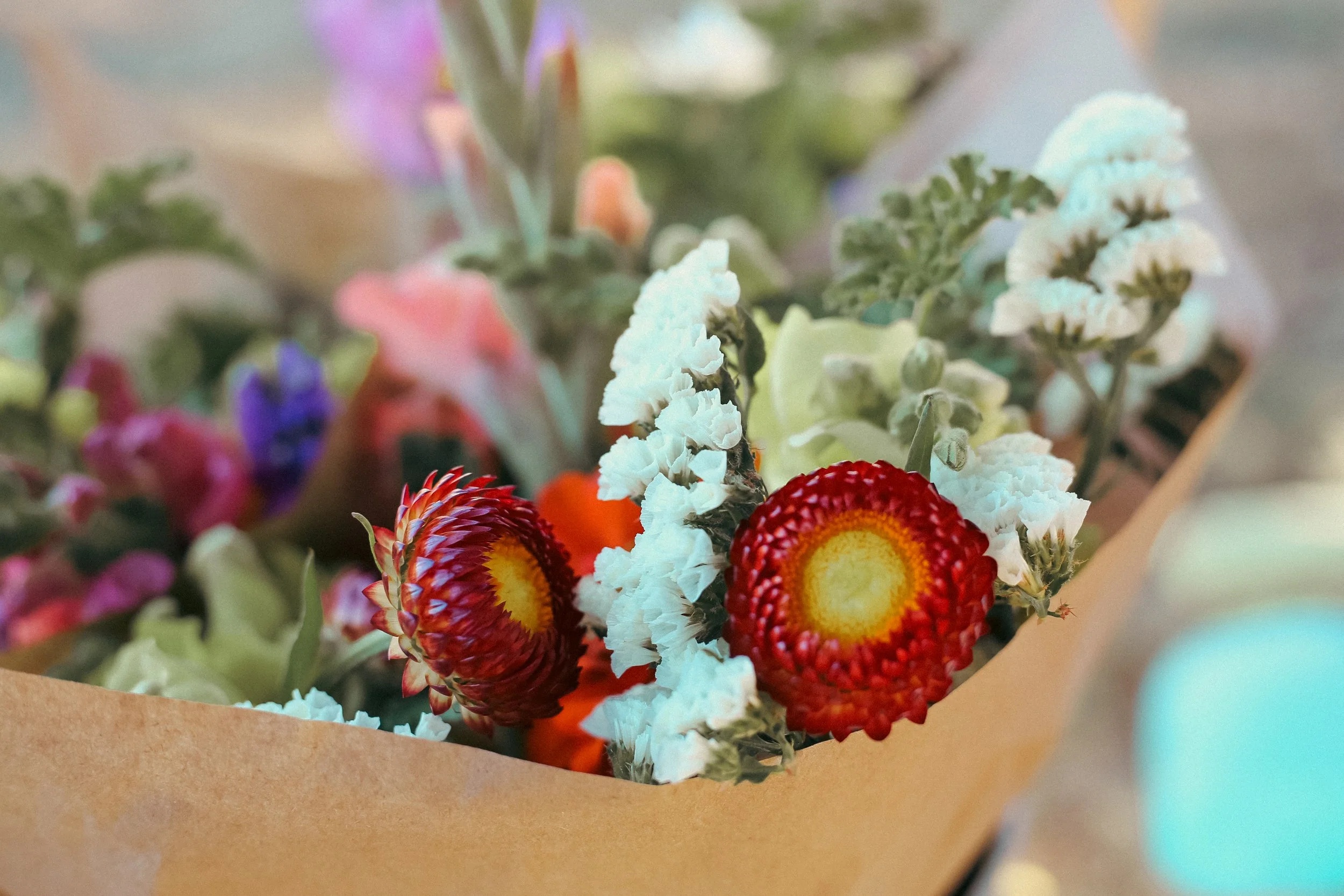 Bouquet of colorful flowers with red, yellow, purple, pink, orange, and white blooms wrapped in brown paper.