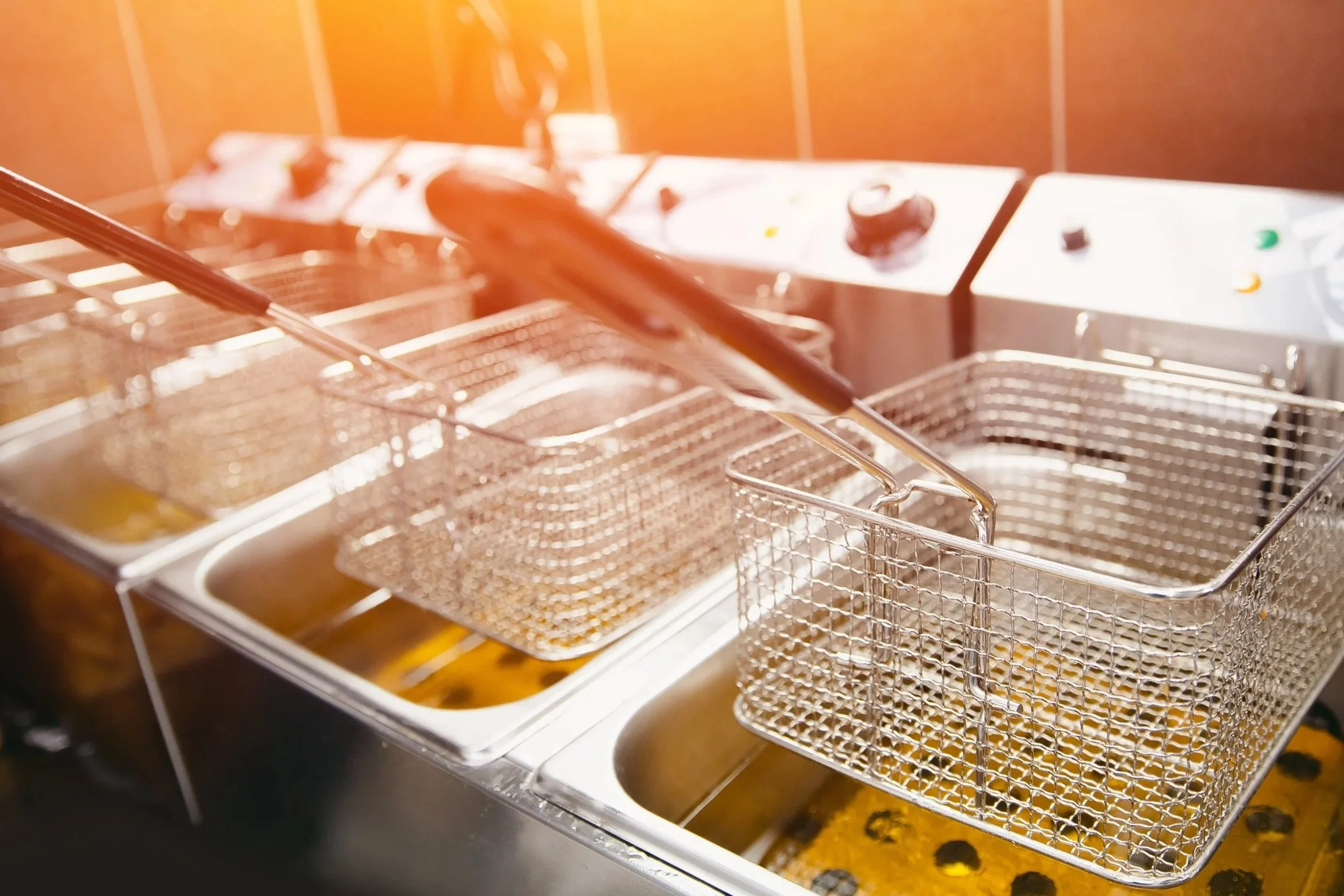 A deep fryer with multiple baskets submerged in oil, used for cooking fried foods in a commercial kitchen.