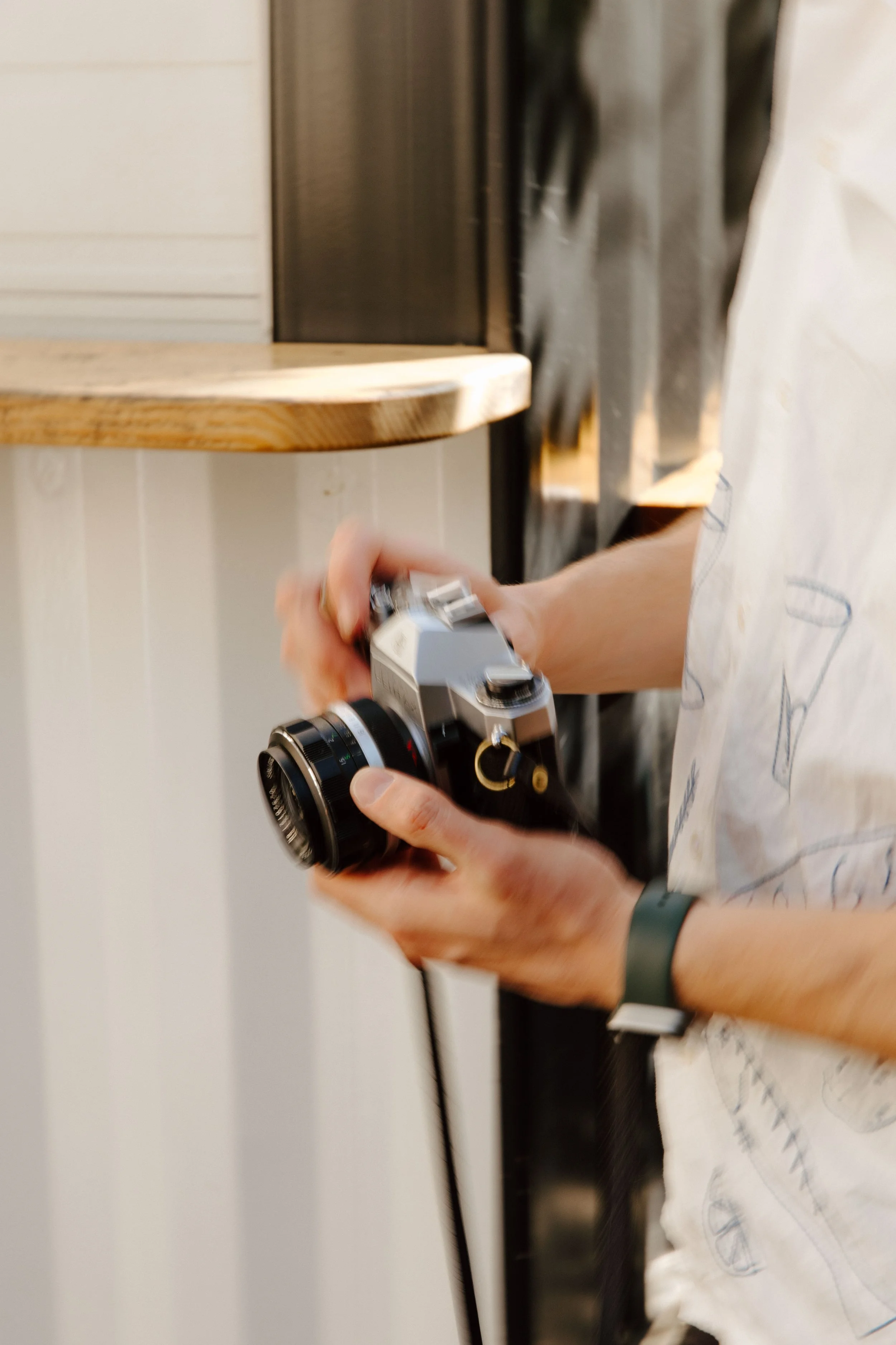 Person holding a vintage film camera indoors, with a wooden shelf and wall in the background.