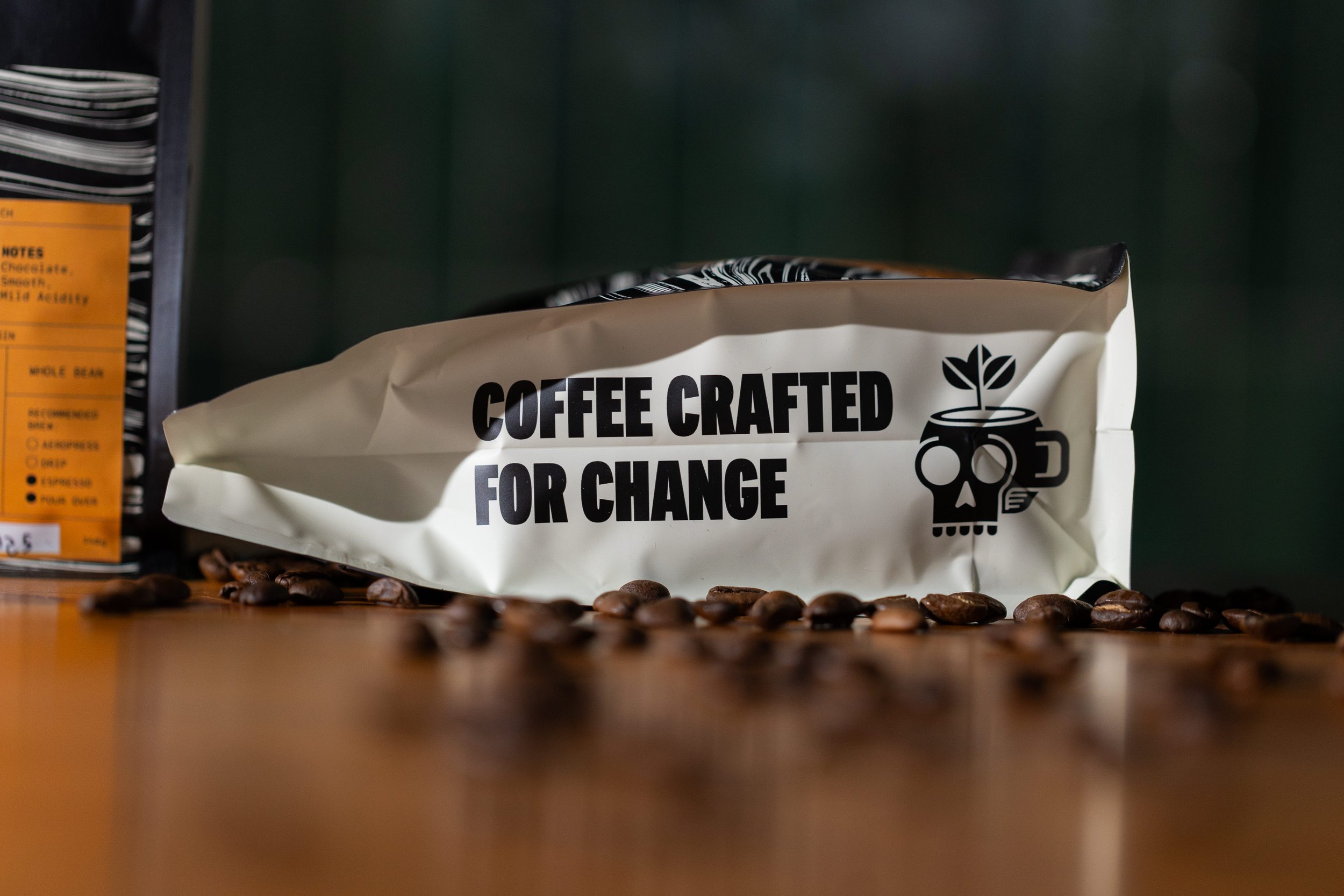A coffee bag labeled 'Coffee Crafted for Change' with coffee beans scattered in front of it, positioned on a wooden surface.