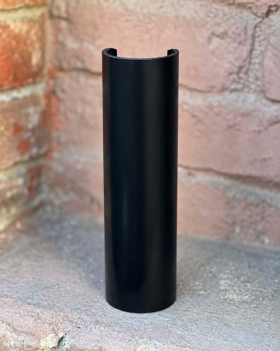 A black RokPro motorcycle fork guard, standing upright on a concrete surface against a brick wall background.