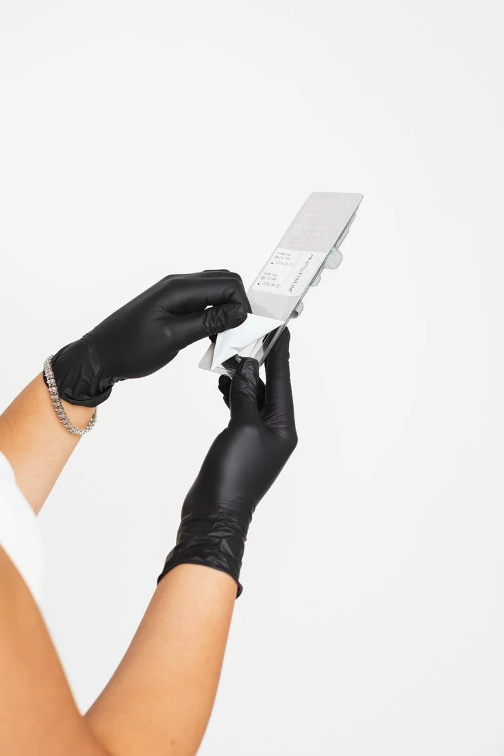 Person wearing black gloves cleaning a receipt from a small electronic device with a cloth, against a plain white background.