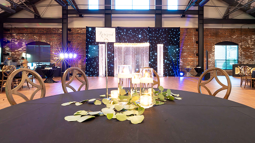 Event venue with round tables, decorated with foliage and candles, and a stage with starry backdrop and lighting.
