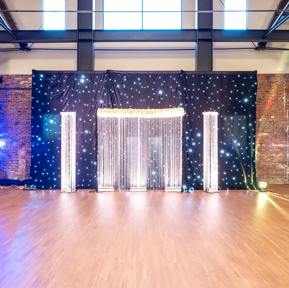Decorative backdrop with fairy lights and fabric, set up on a wooden floor for an event or celebration.