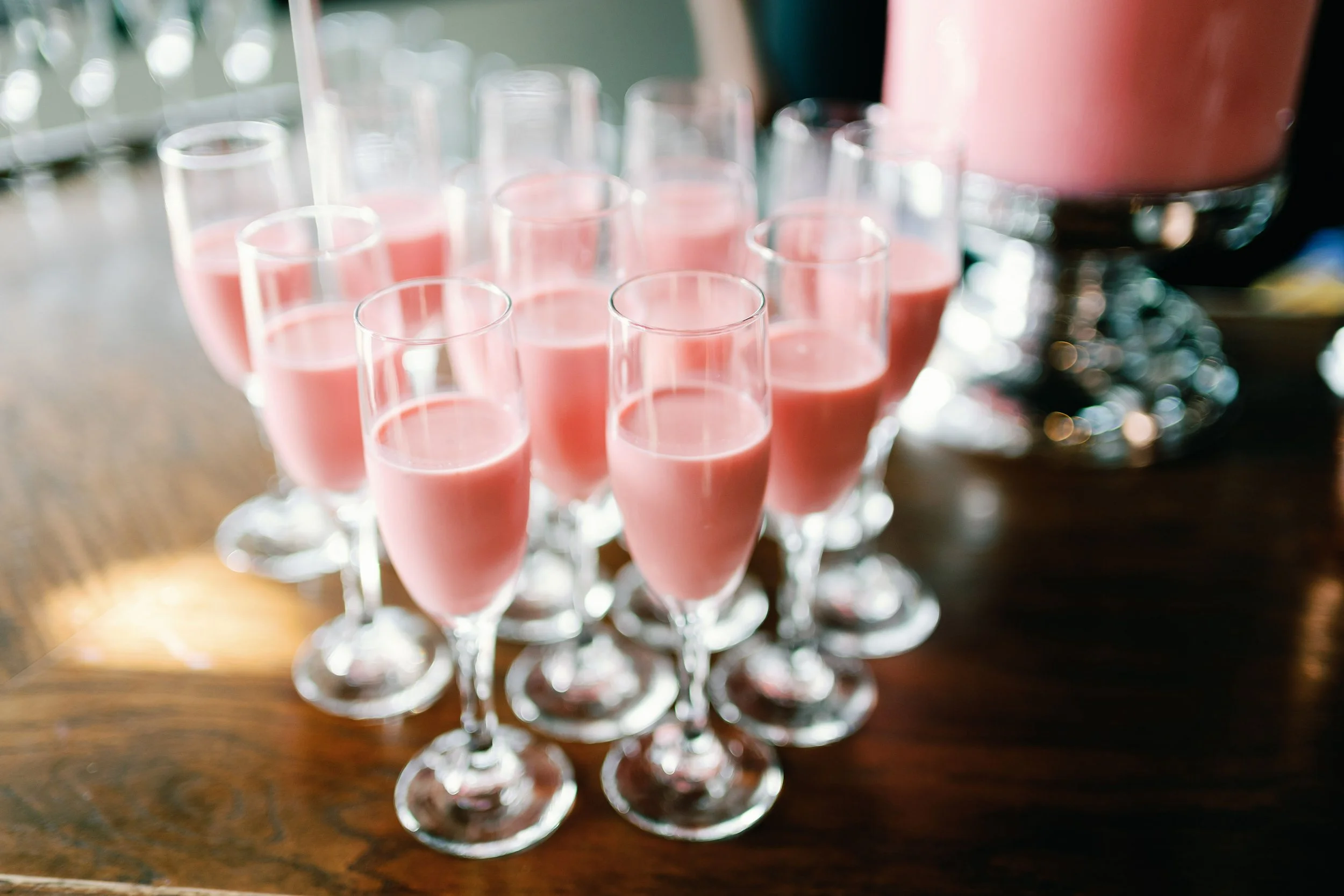 Multiple champagne flutes filled with pink beverage, arranged on a wooden surface.