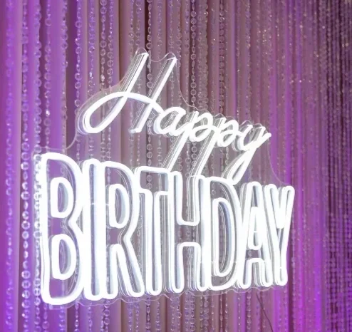 Neon sign that says 'Happy Birthday' with purple hanging curtain background.