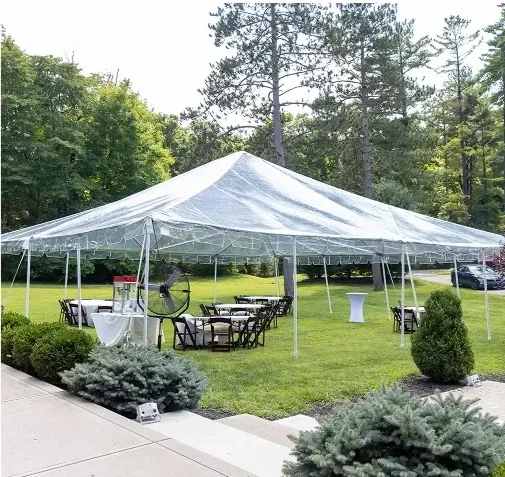 Large white outdoor event tent set up on a grassy lawn with chairs, tables, and a white table with a red and white cake, surrounded by trees.