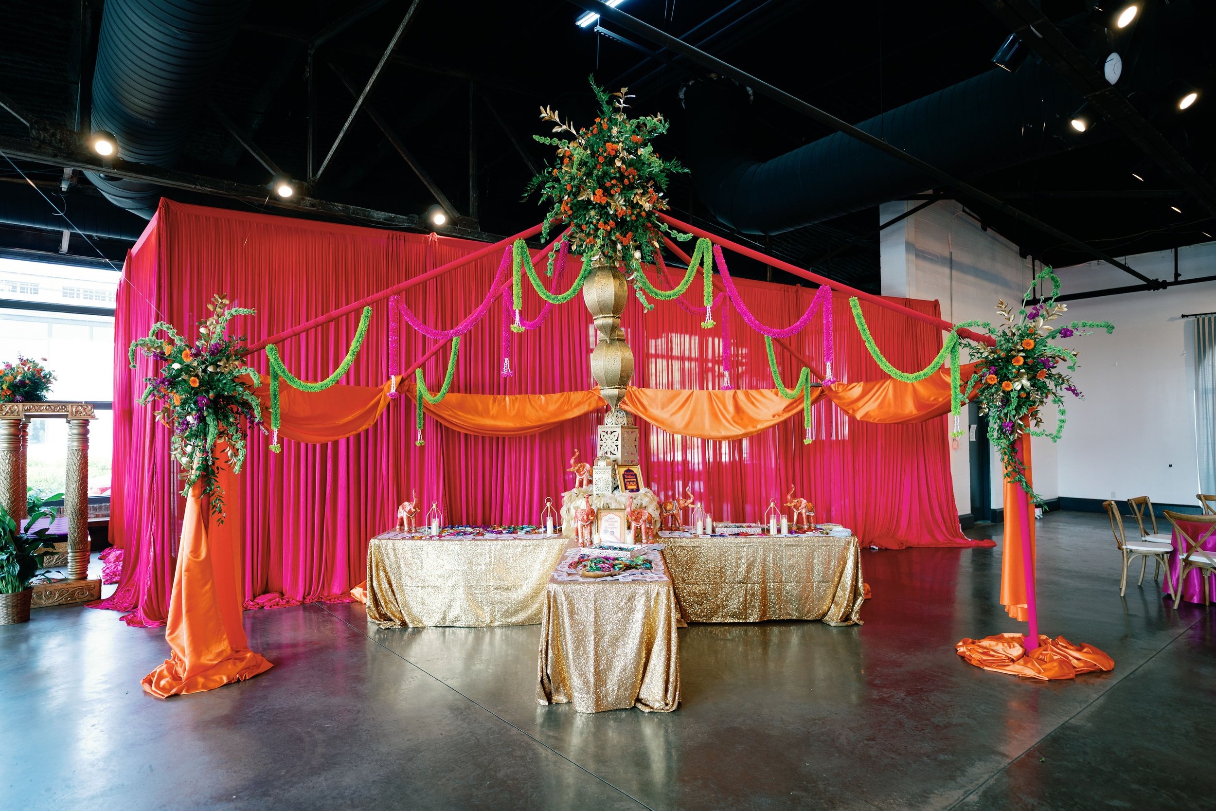 Decorated event stage with pink and orange drapes, floral arrangements, and elephant figurines, set for a celebration or cultural ceremony.