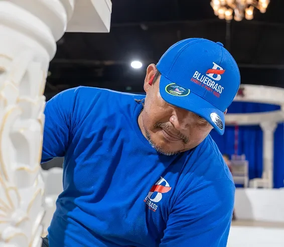A man wearing a blue Bluegrass logo cap and blue shirt, working indoors.