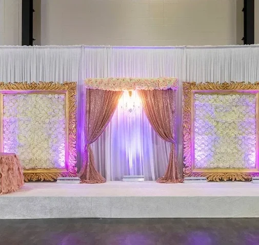 Elegant wedding stage with gold-framed floral panels, pink and brown curtains, and purple lighting.