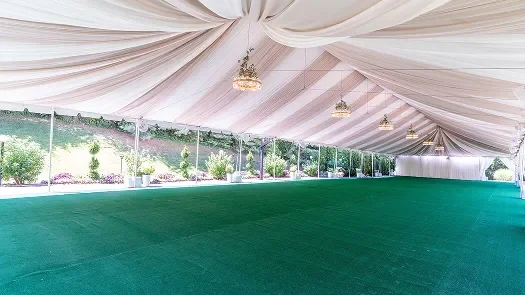 Empty event tent with white draped ceiling and green carpet floor during daytime