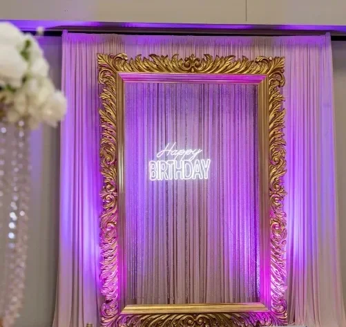 Decorative birthday backdrop with a gold ornate frame, purple lighting, and a neon sign that says 'Happy Birthday'.