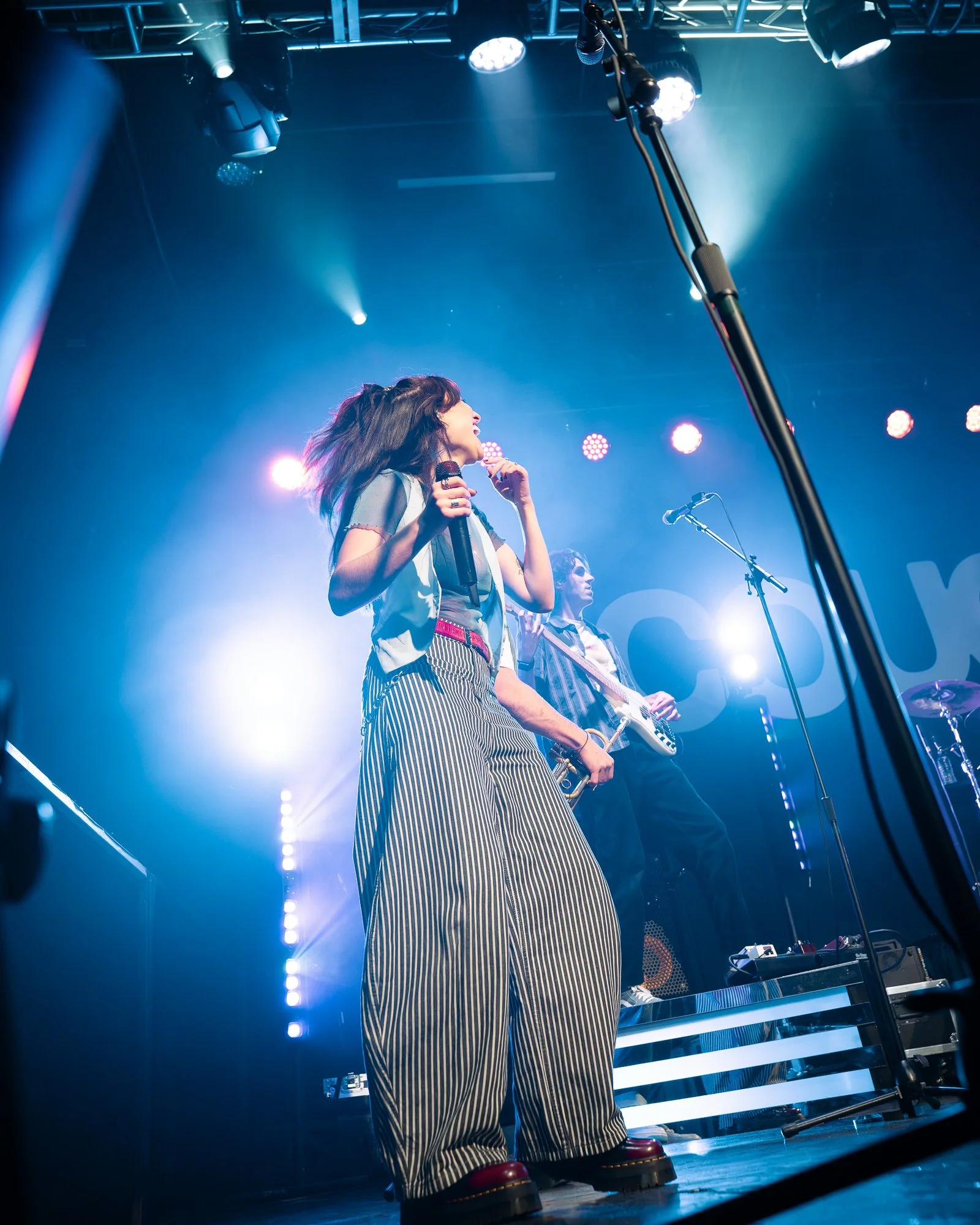 A female singer and a male musician performing on stage under colorful lights at a concert.