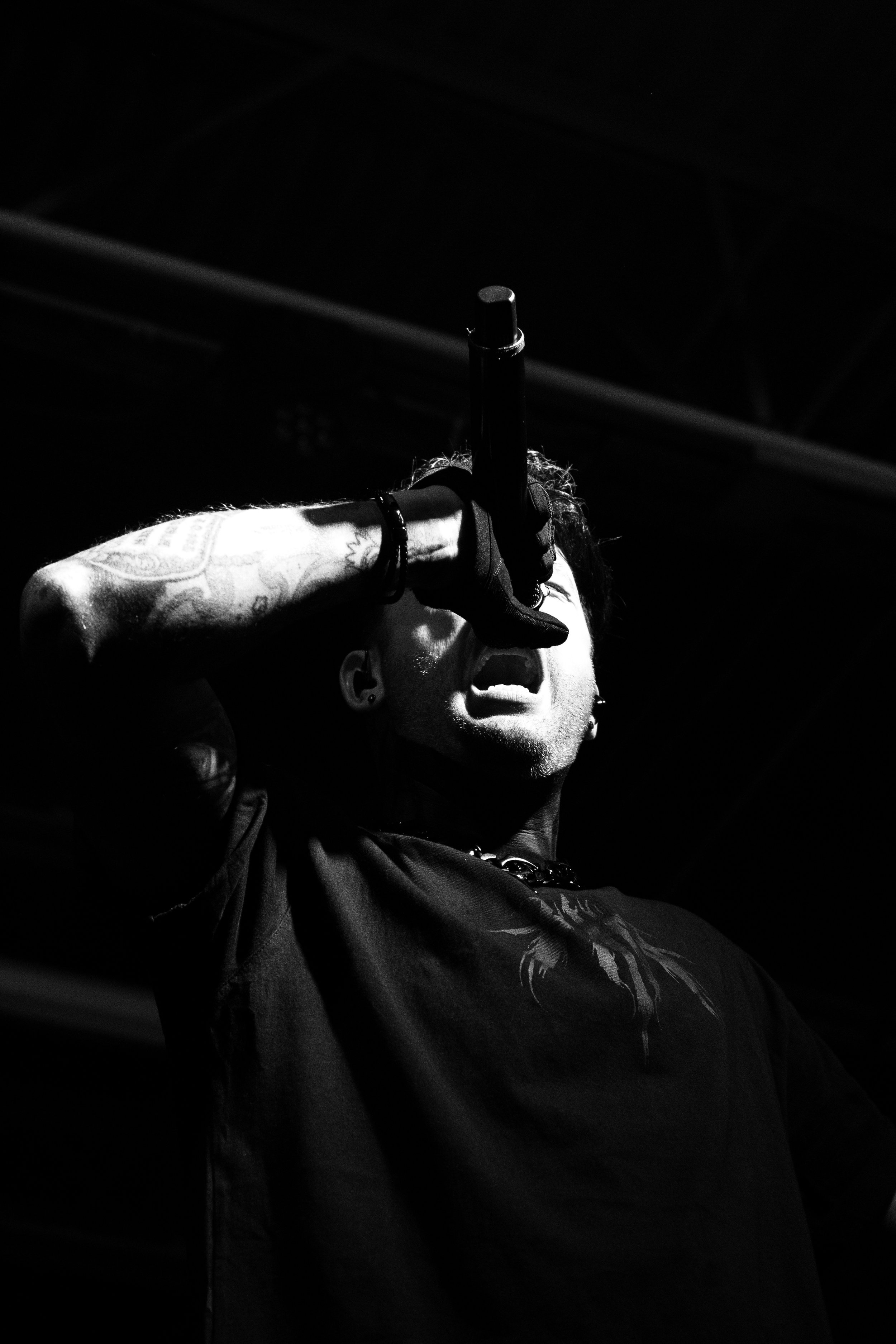 Male singer performing on stage, holding a microphone close to his mouth, with intense expression, wearing a dark shirt, in a black and white photograph.