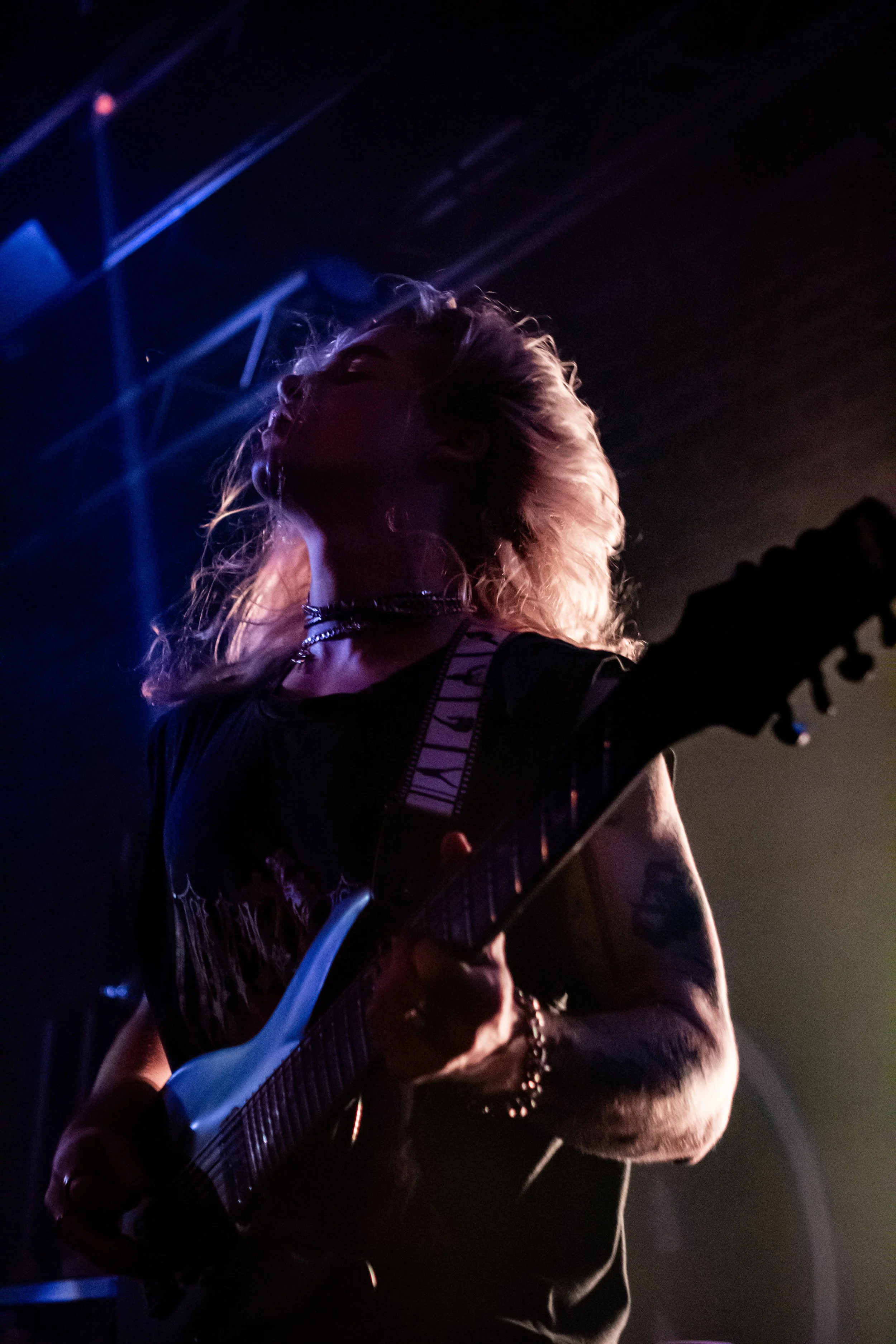 A woman playing an electric guitar on stage with stage lights shining behind her, creating a silhouette effect.