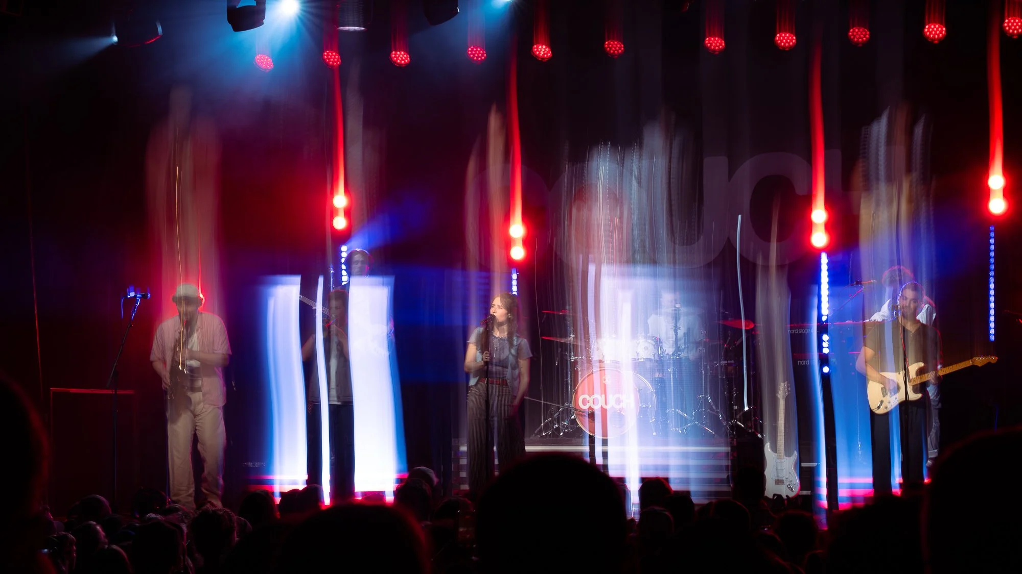A band performing on stage with colorful lighting effects and motion blur, including singers and guitarists.