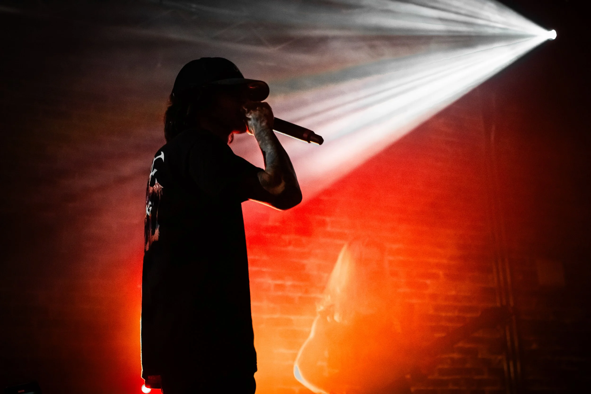 Silhouette of a person with a microphone, standing with a spotlight illuminating from the side, with a brick wall background.