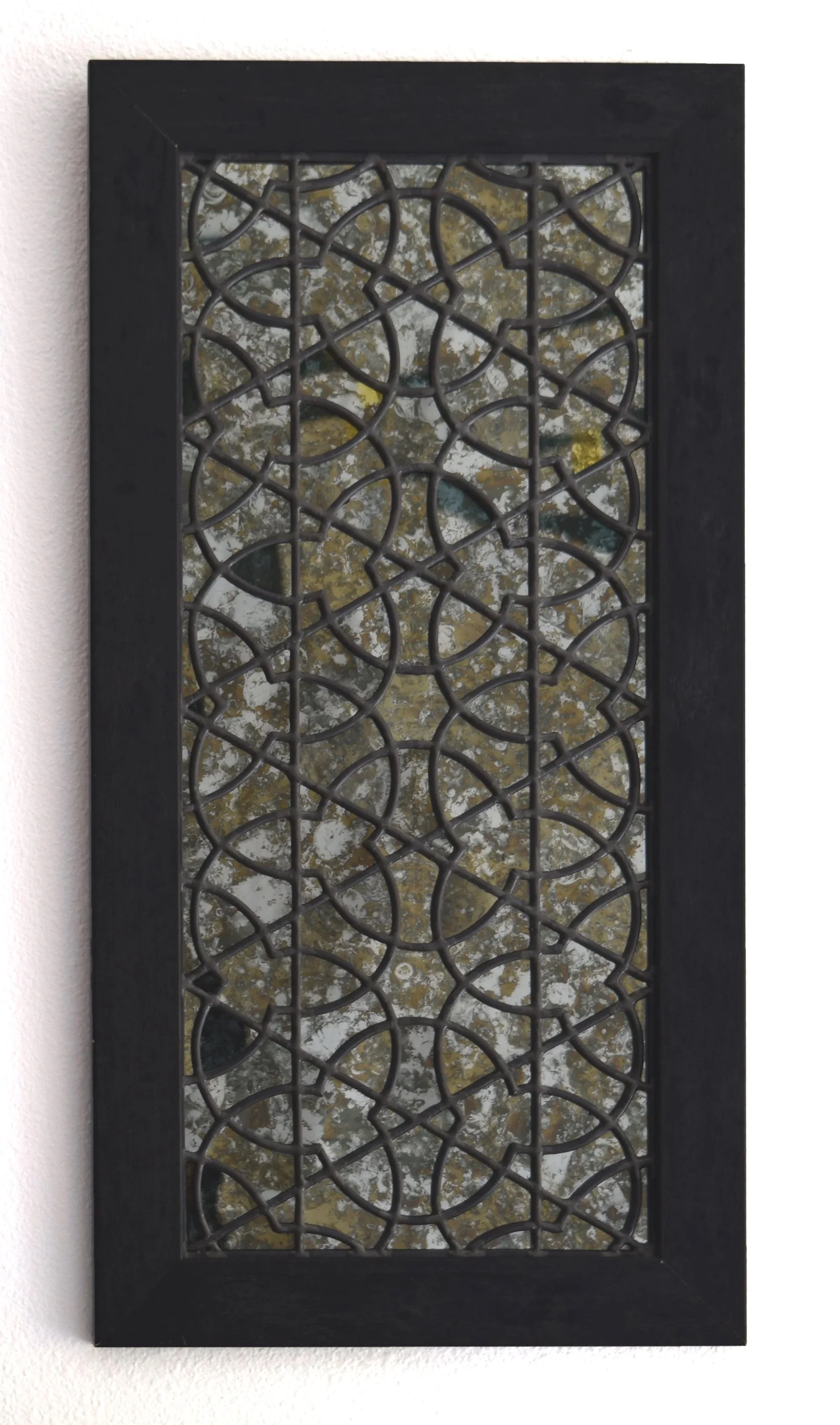 Decorative mirror with an ornate metal lattice design reflecting trees with autumn leaves.