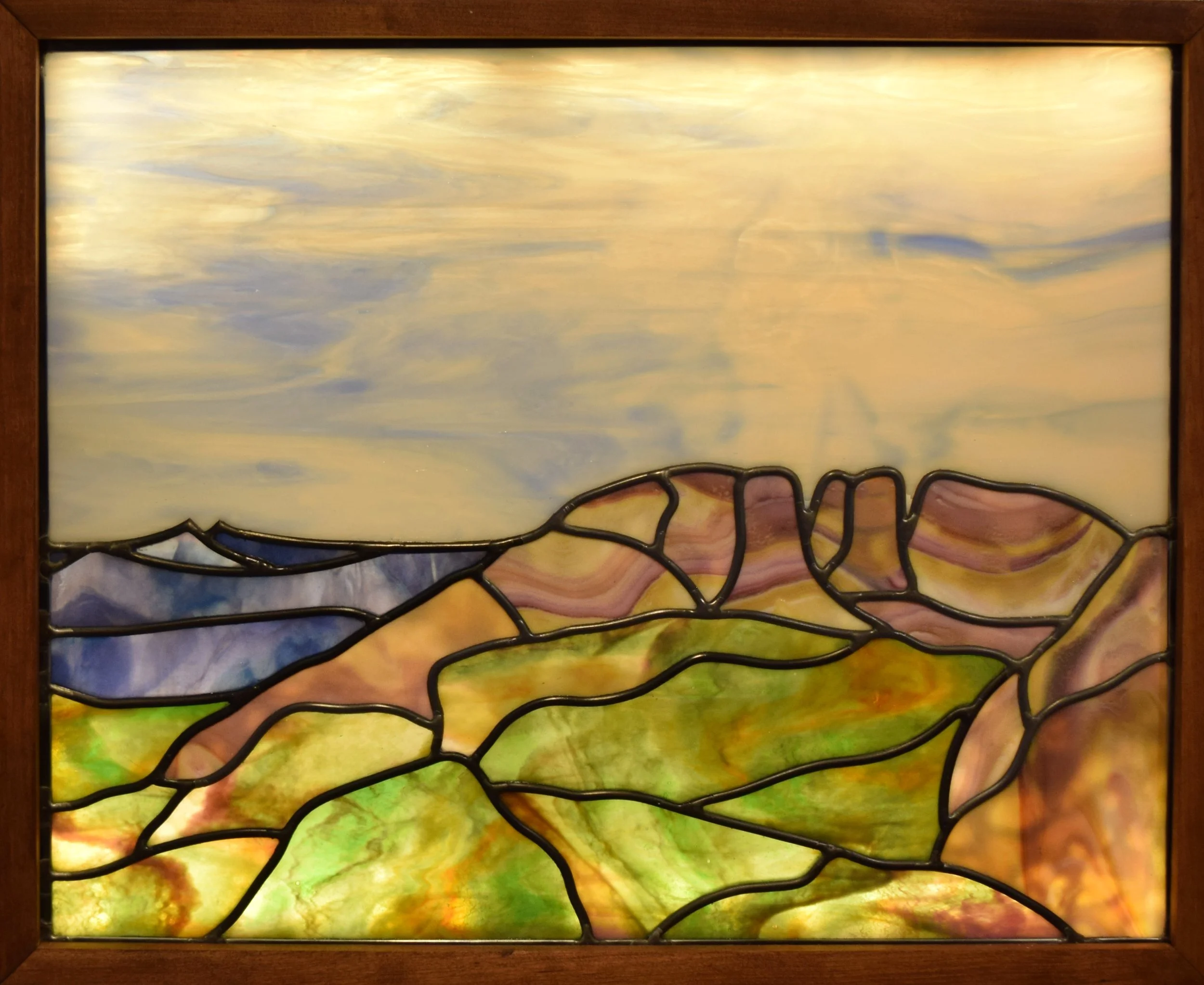 Colorful custom stained glass window with abstract landscape design of Horsetooth Mountain in Fort Collins, Colorado framed in wood.