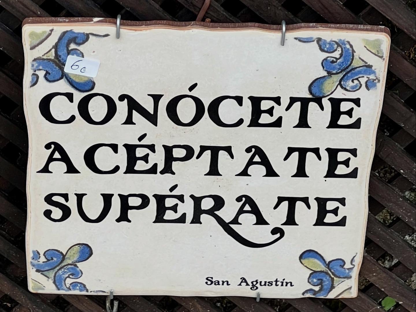 A decorative sign with blue and yellow floral accents, reading 'Conócete Aceptate Superate' in bold black letters, located in San Agustin.