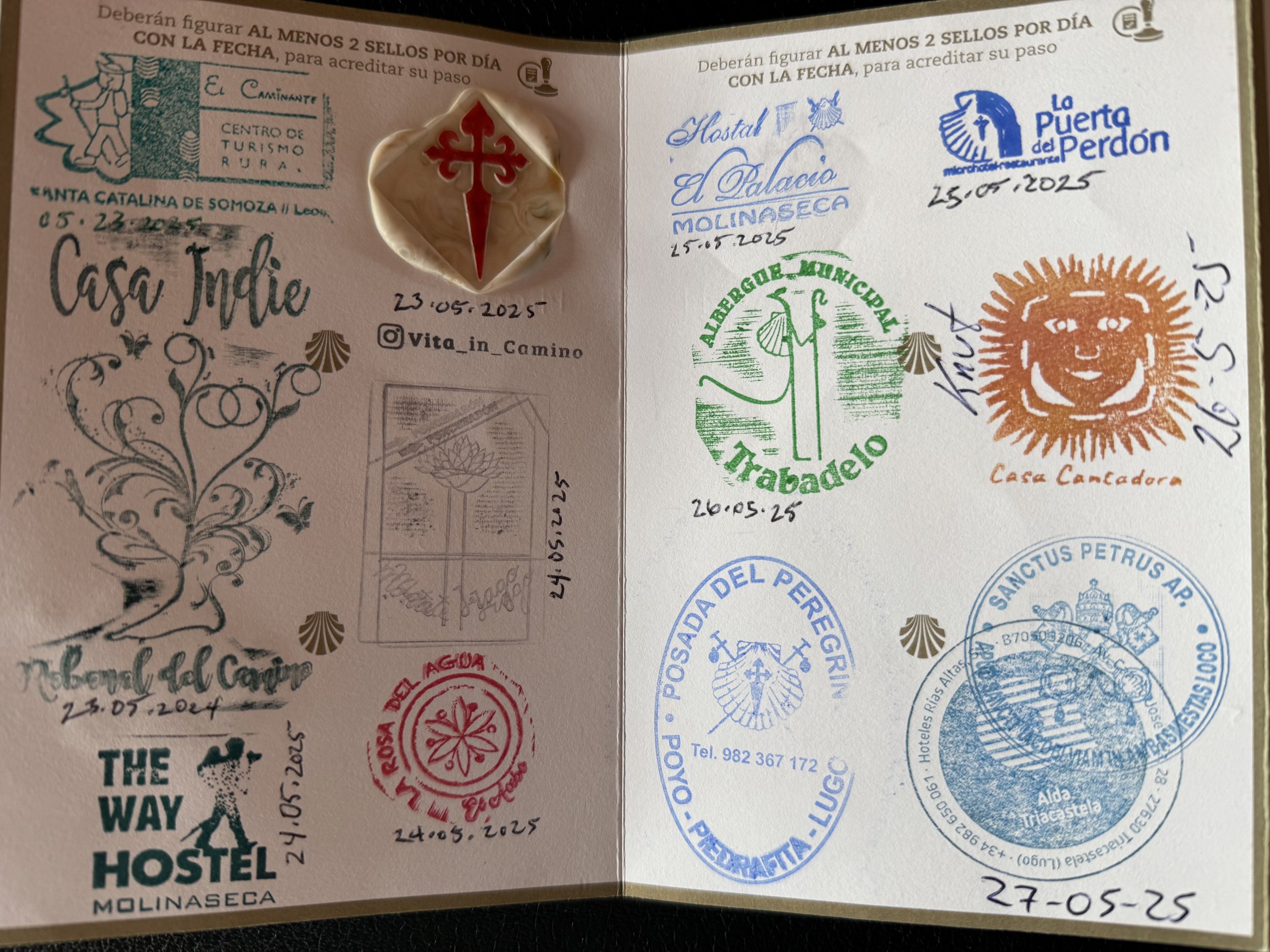 Open passport or travel journal showing various stamps and signatures from different locations, dates, and hosts, including a prominent red cross symbol, handwritten notes, and decorative elements.