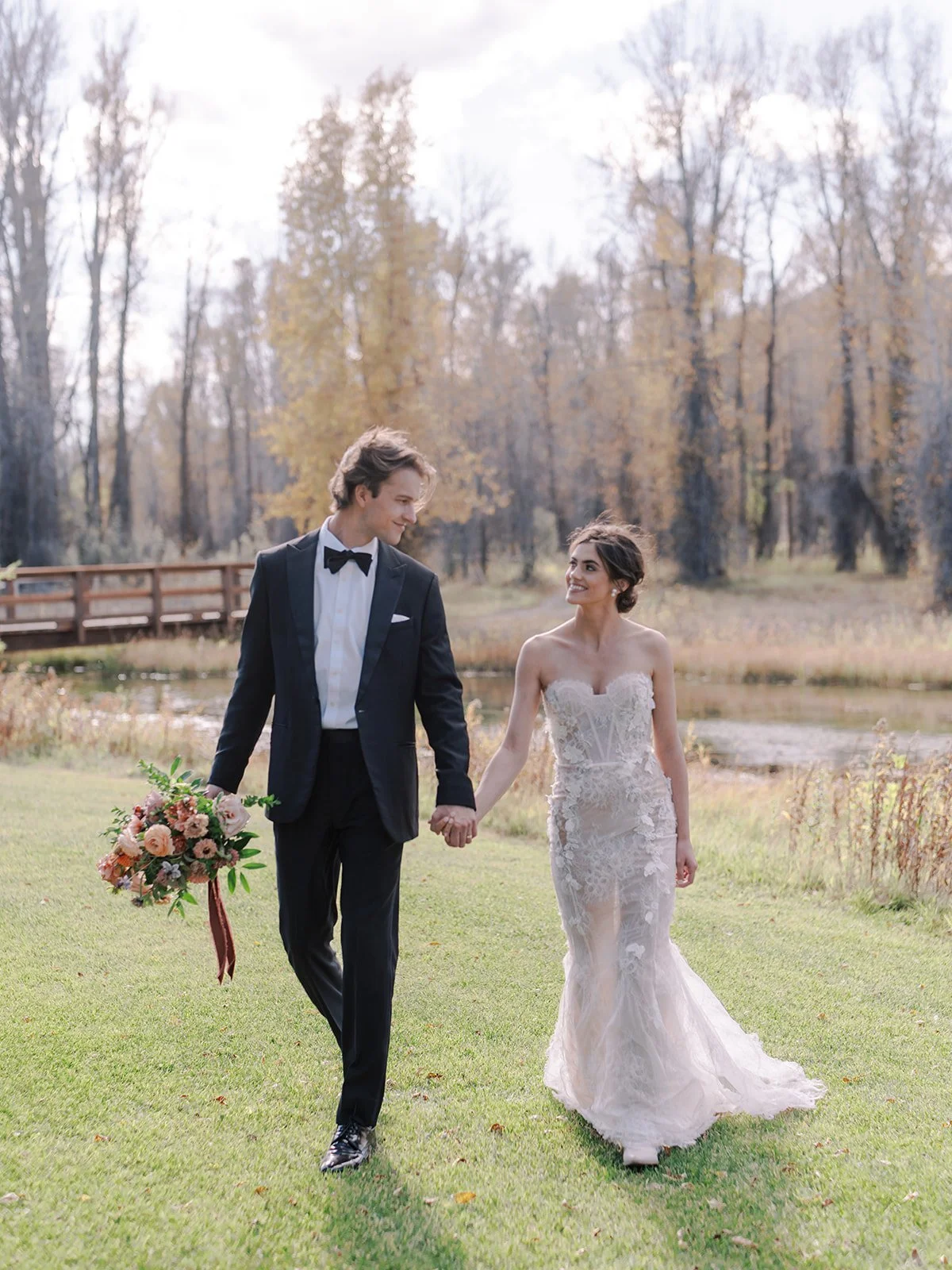 Bride and groom walk hand in hand through a forest meadow during their Jackson Hole wedding.