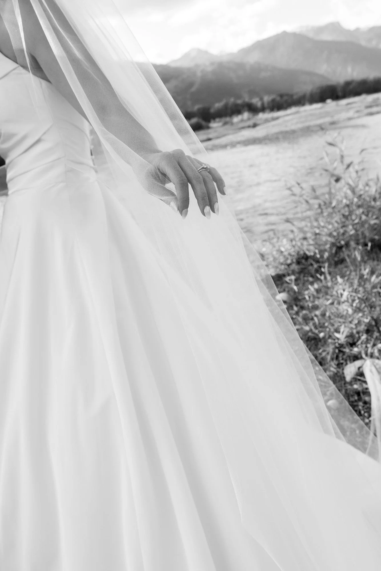 A close-up of a bride in a wedding dress with a veil, outdoors with mountains in the background.