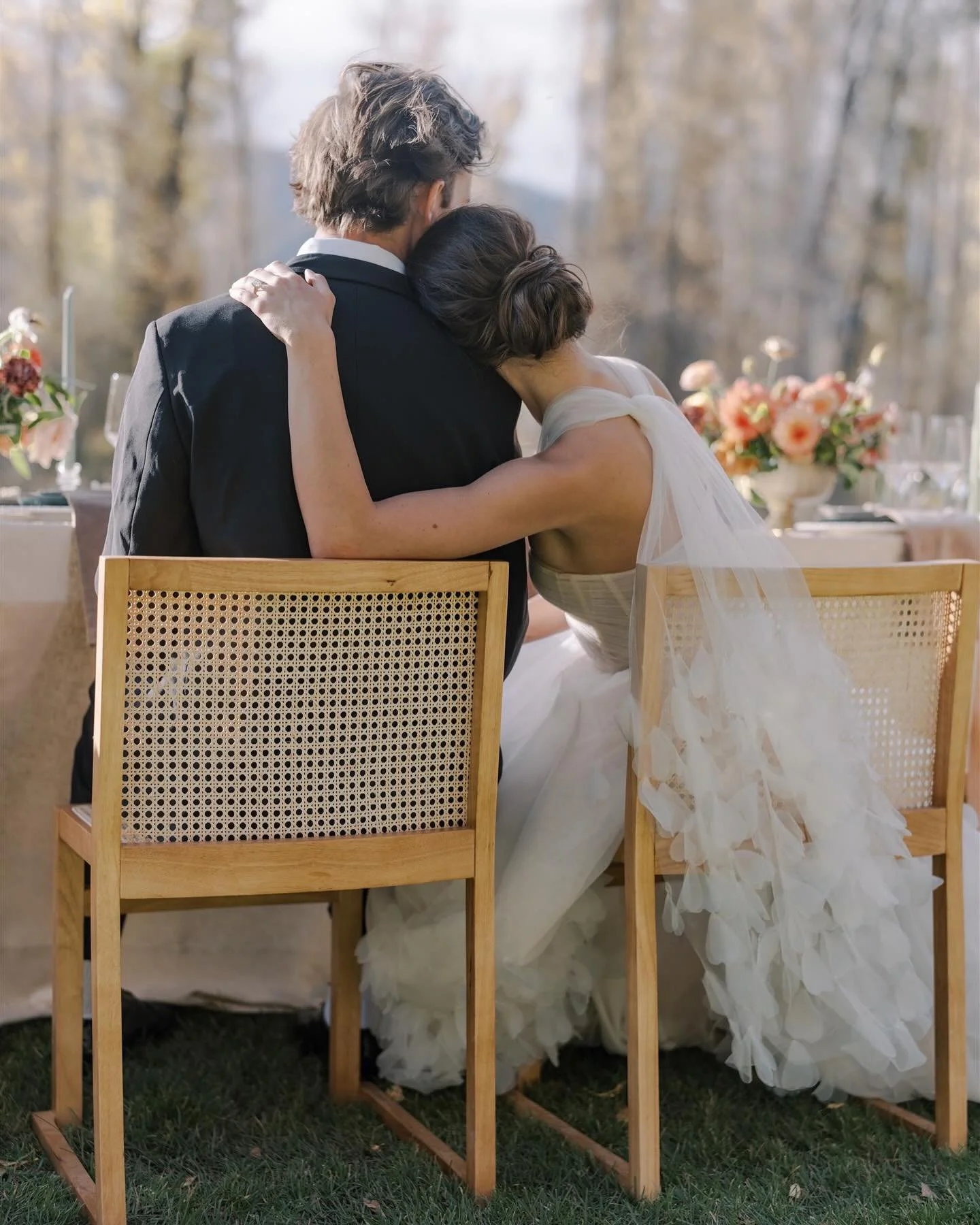 Bride rests her head on the groom’s shoulder during their Jackson Hole wedding reception with floral table décor.