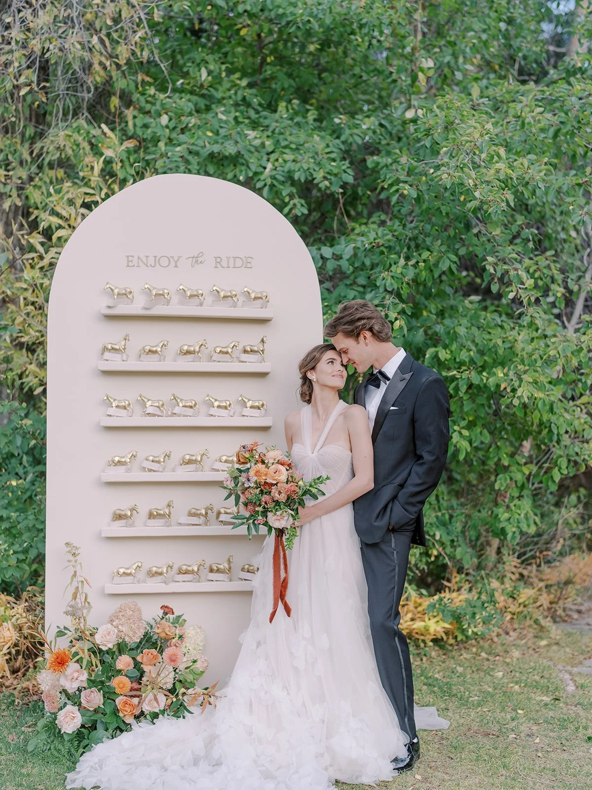 Bride and groom pose beside a creative escort card display reading “Enjoy the Ride” at their Jackson Hole wedding.