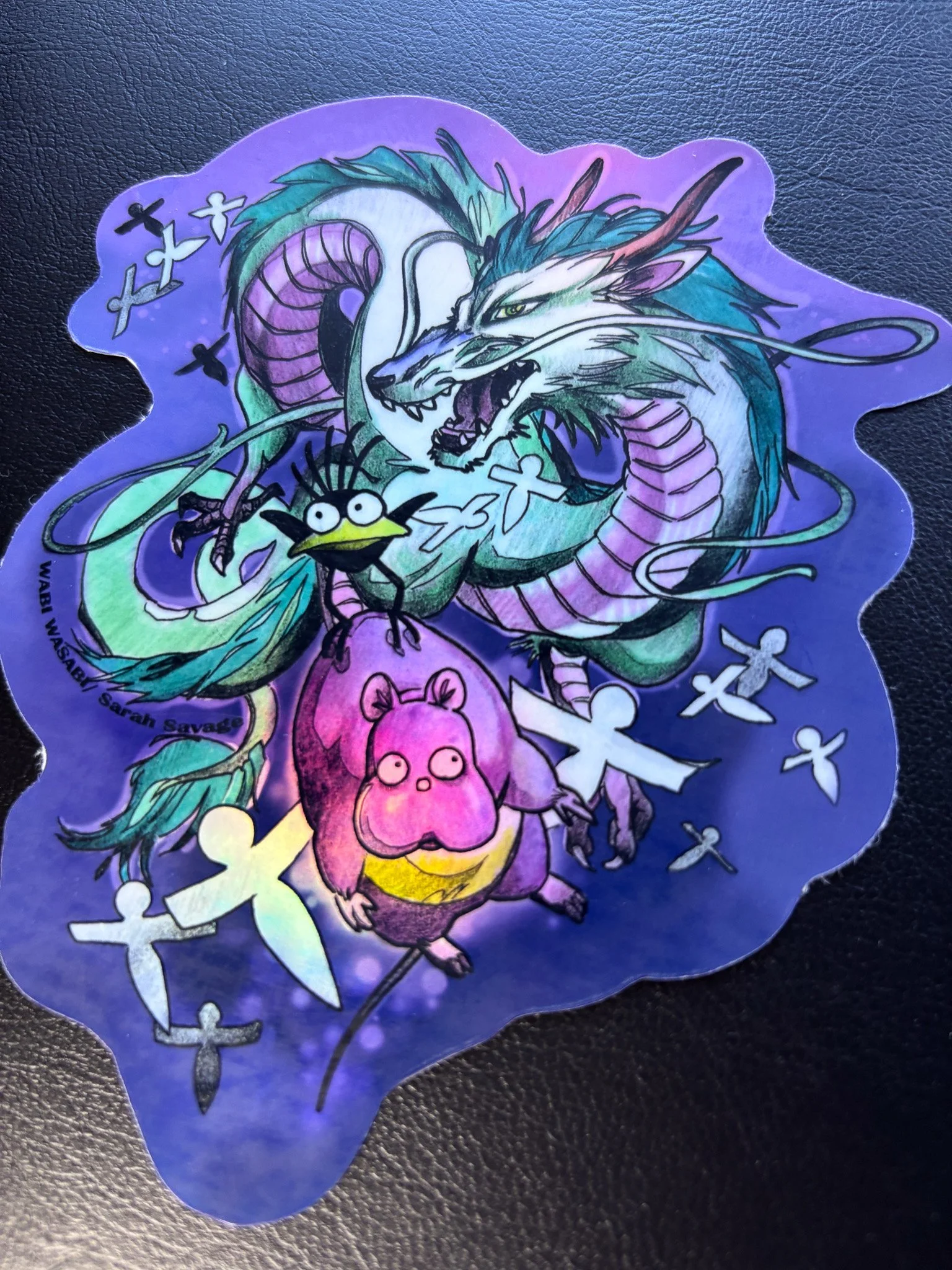 Colorful sticker featuring a dragon, a small bird, and a pink rat, surrounded by white angel and cross symbols with a purple background.
