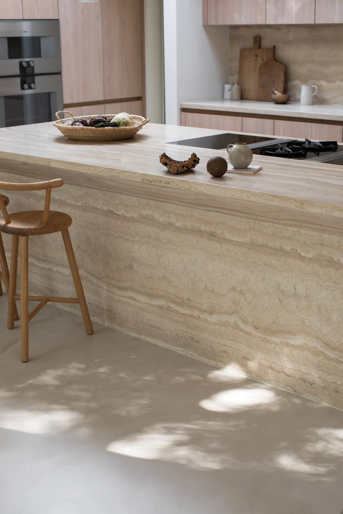 Modern kitchen with beige stone island, wooden chairs, and minimal decorative items on the counter.