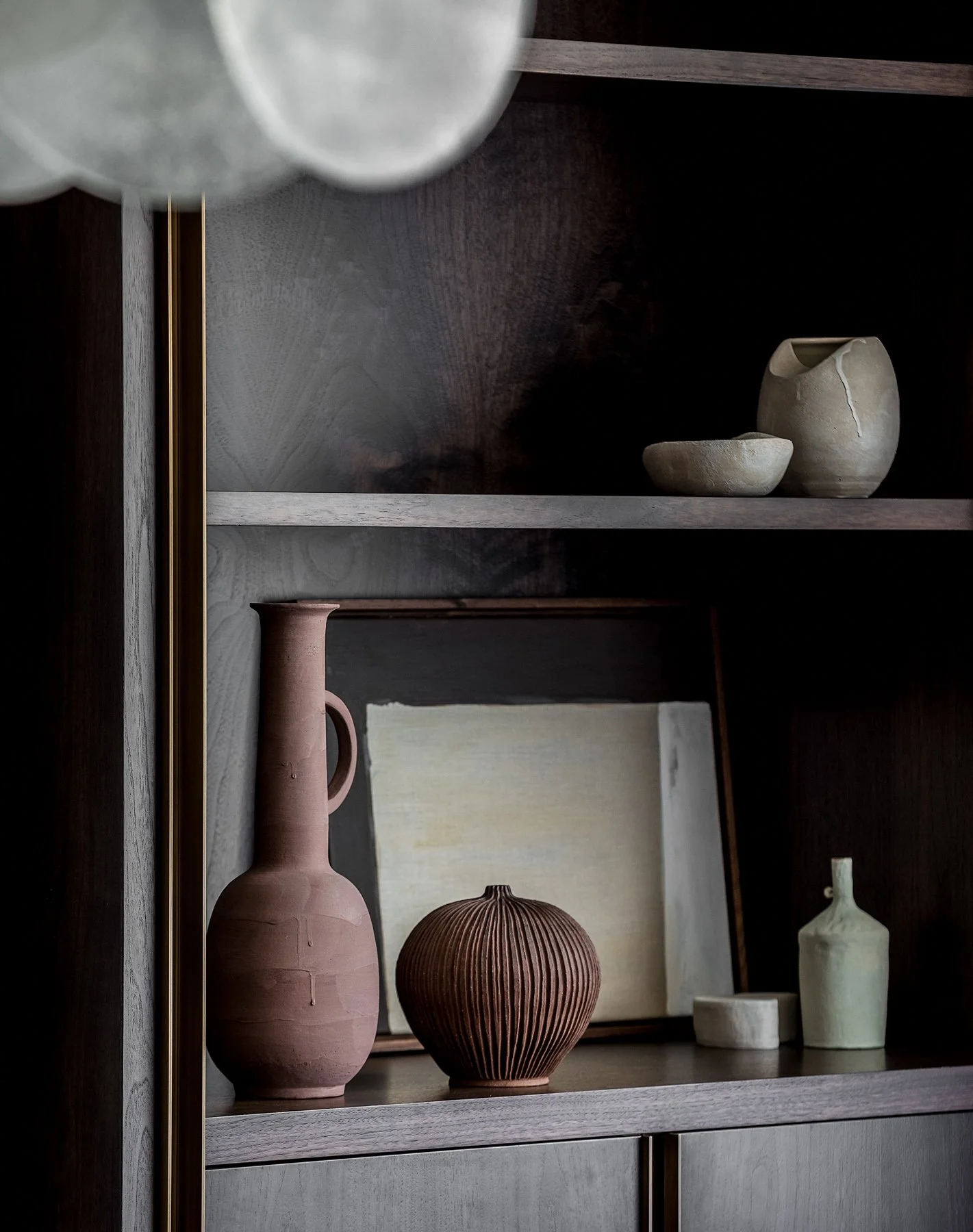 Decorative ceramic vases and bowls on a wooden shelf with a framed artwork in the background.