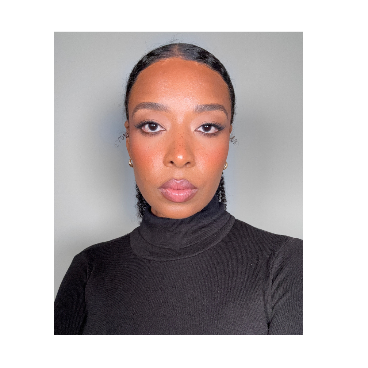 A professional woman with a warm smile, dark curly hair pulled back, wearing a navy blazer and white top, standing against a light gray background.