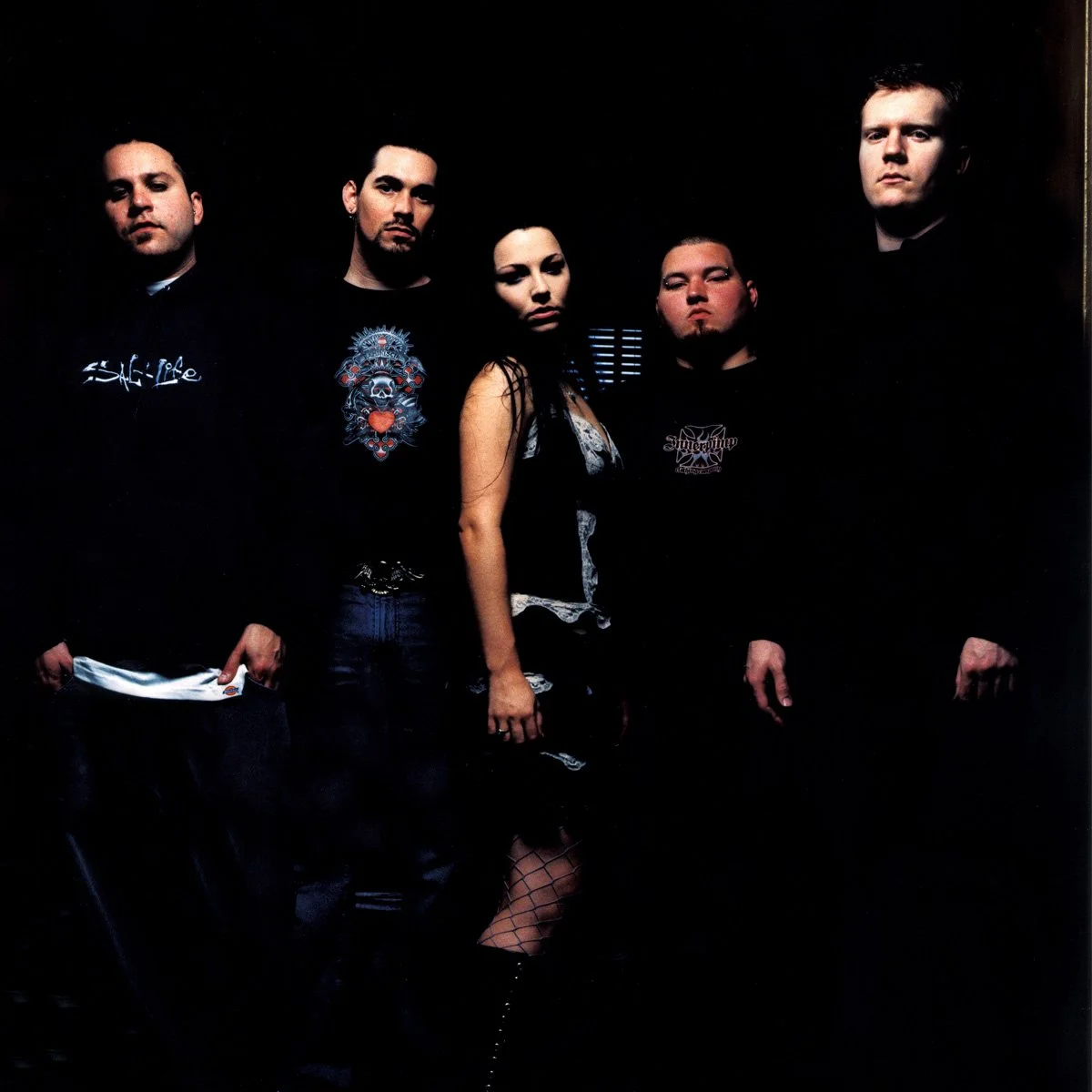 Five people standing indoors, three men and two women, with dark background.