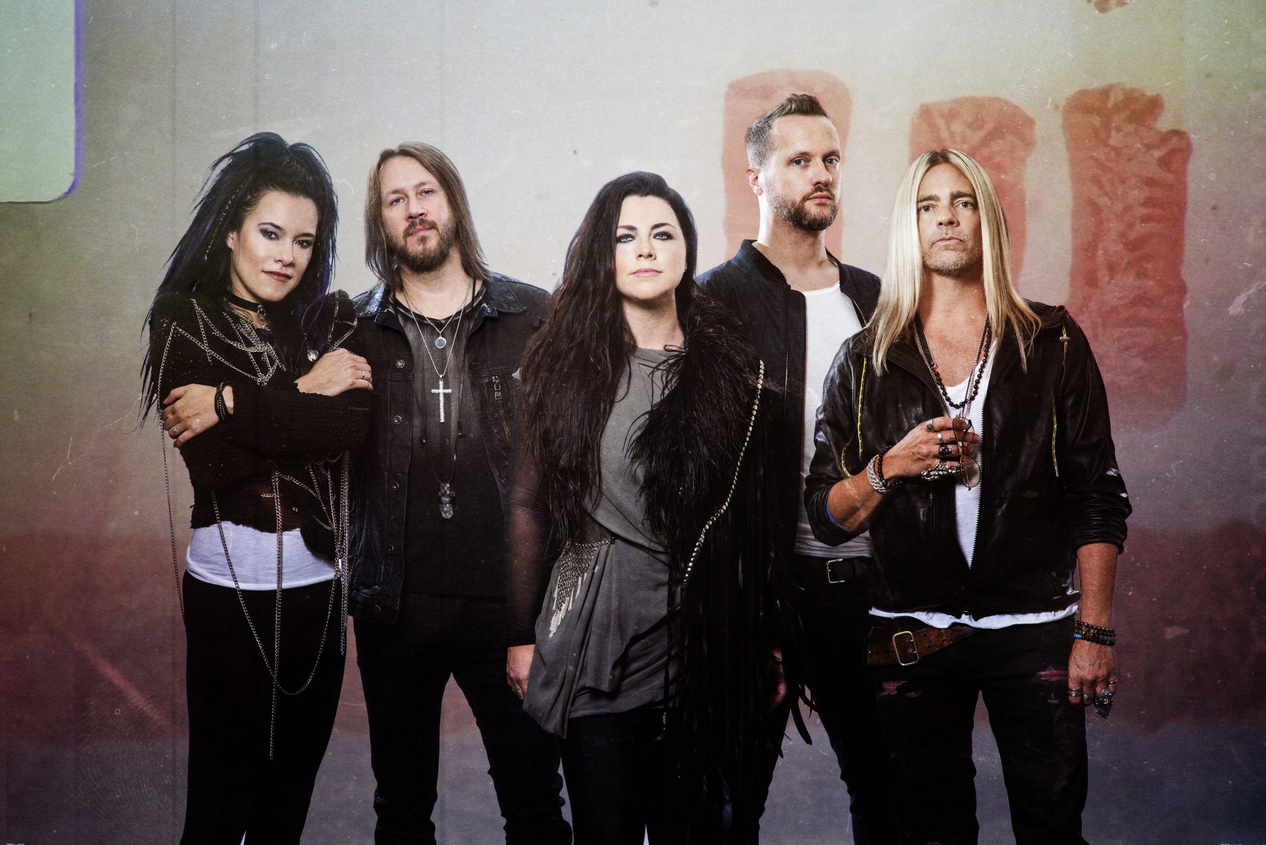 A group of six musicians posing together, dressed in black and gray clothing, with intense expressions, in a photo with a colorful background.