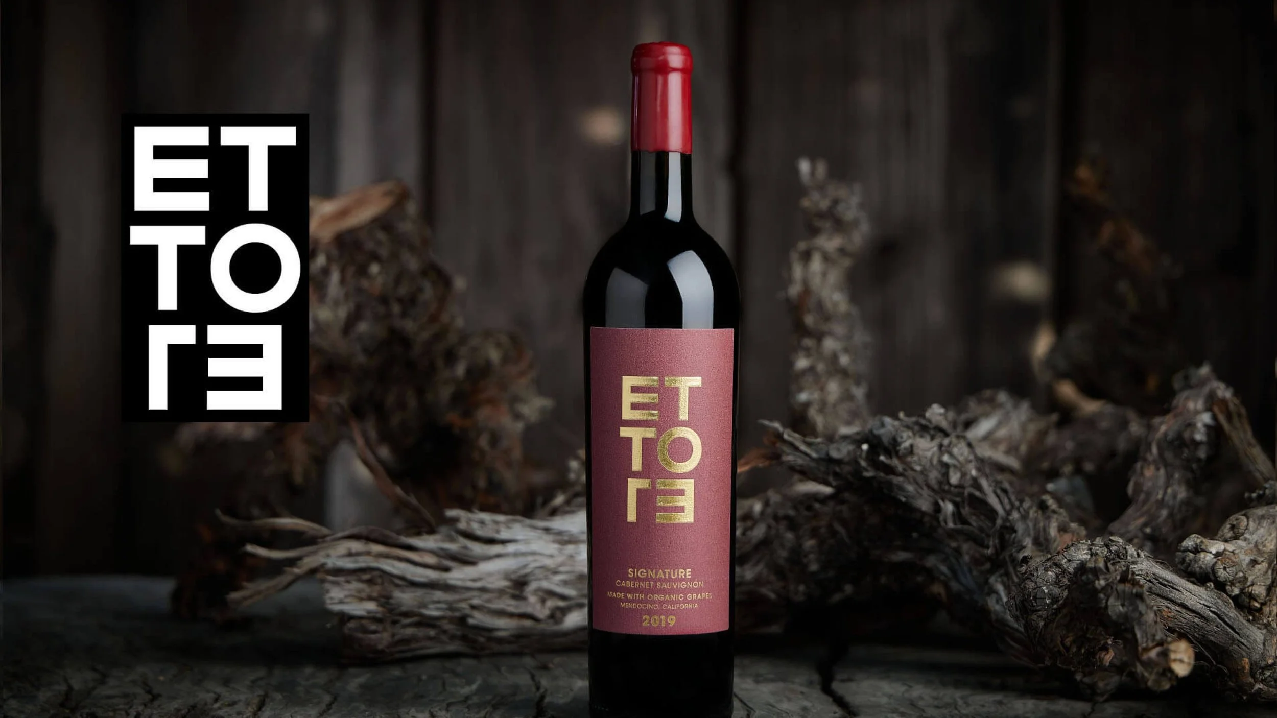 A bottle of red Ettore Cabernet Sauvignon wine with a maroon label and gold text, set against a rustic wooden background with pieces of wood around it.