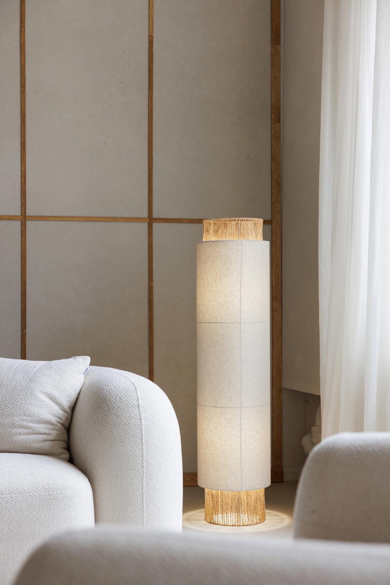 Ein hell leuchtender Stehlampe in einem modernen Wohnzimmer, mit cremefarbenen Sofas und einem hellen Vorhang.