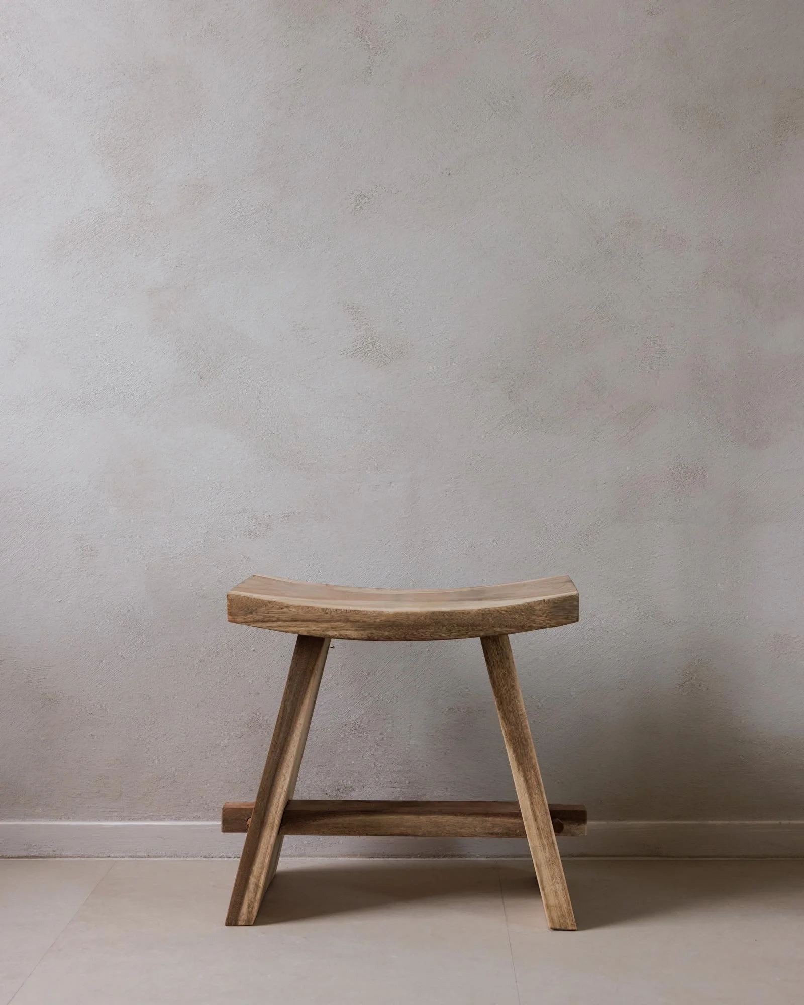 Ein kleines, hölzernes Sitzmöbel vor einer hellgrauen Wand