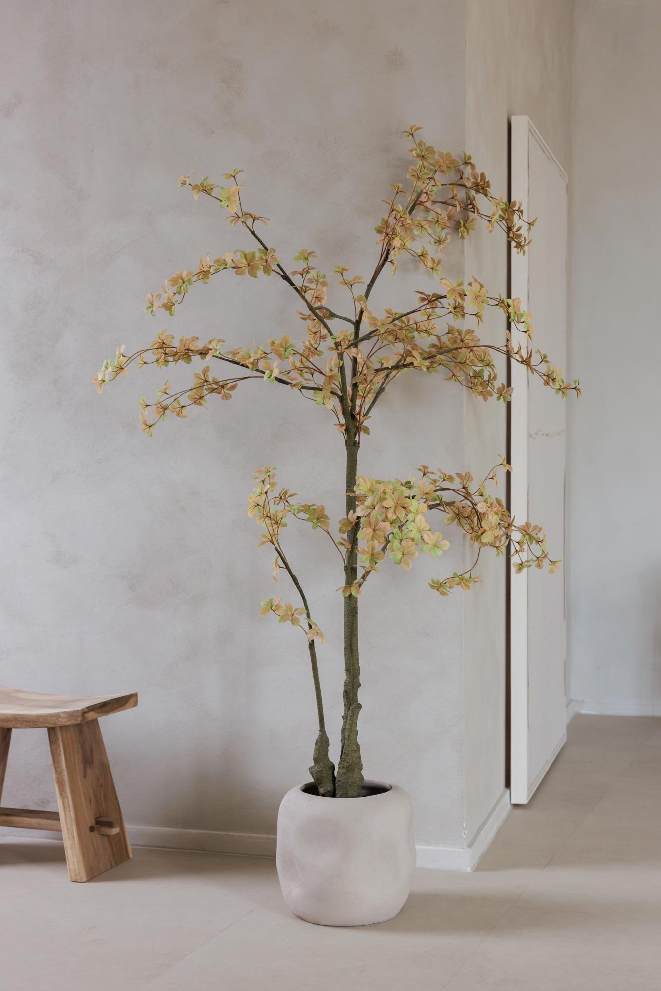Künstlicher Baum in einem weißen Topf vor einer hellen Wand