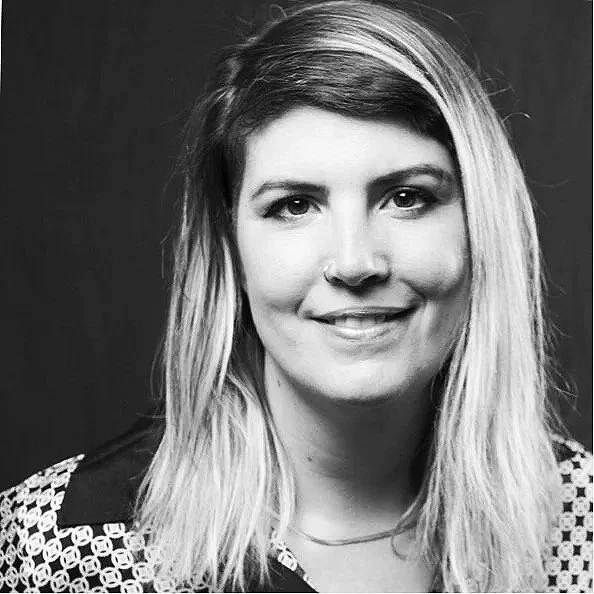 Schwarz-weiß-Porträt einer jungen Frau mit langem, gewelltem Haar, die lächelt, vor dunklem Hintergrund.