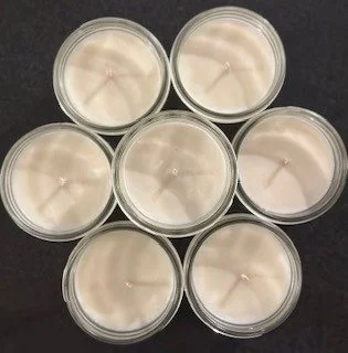 A variety of soy wax candles in small glass jars arranged in a circular pattern with a range of scents available.