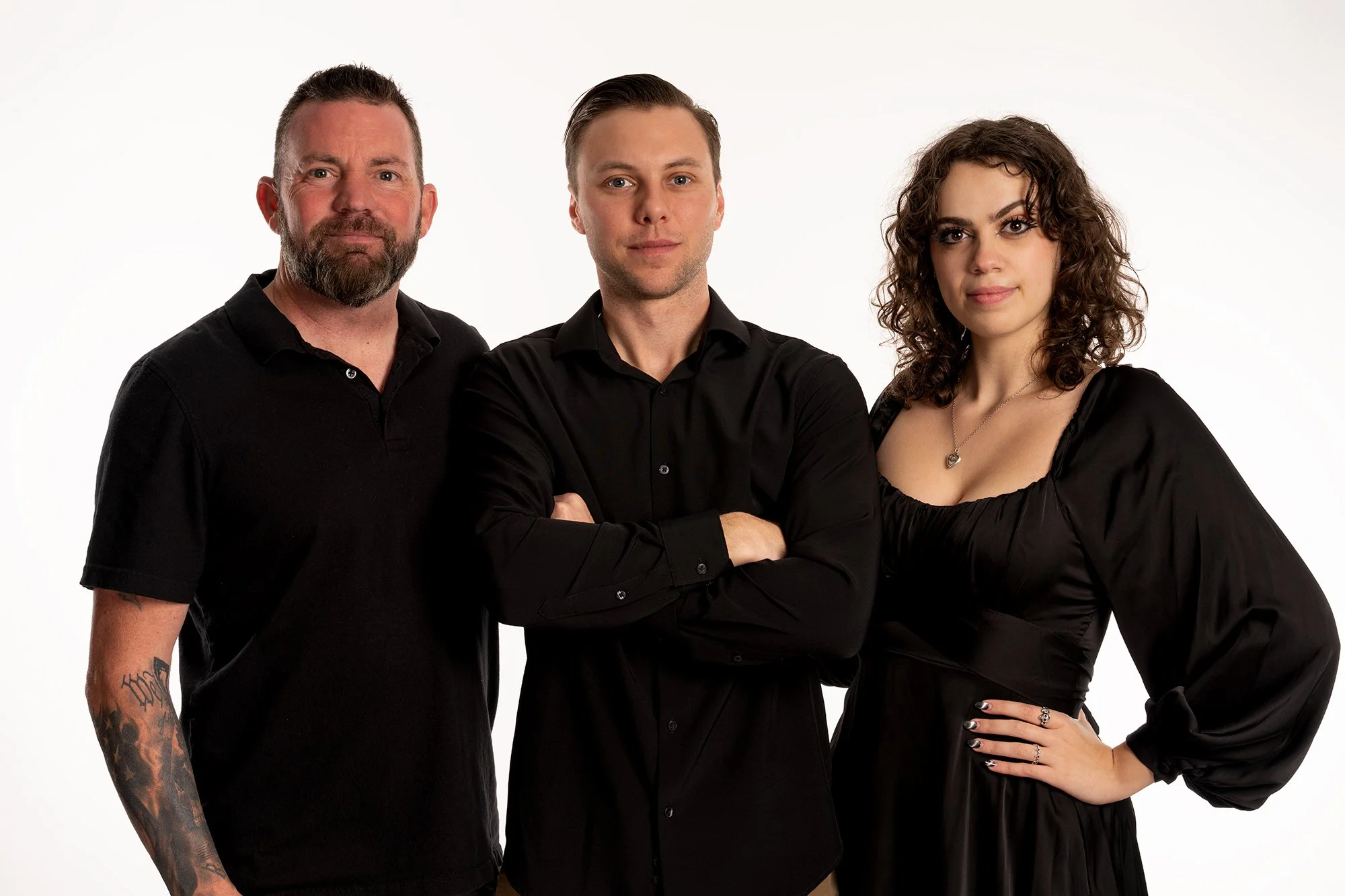 Three people standing close together against a white background, wearing black clothing.