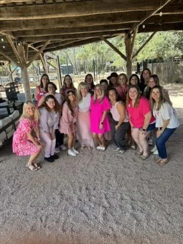 Group of women and girls posing together under a wooden shelter outdoors.