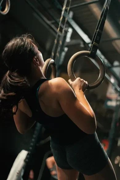 A woman performing a workout using gymnastic rings in a gym setting.