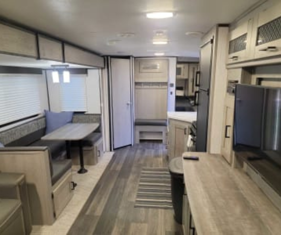 Interior of a modern RV with a dining area, kitchen, and storage cabinets.