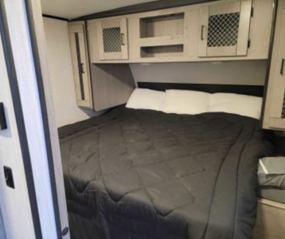 A bedroom with a bed covered in a black comforter, white pillows, and built-in overhead cabinets with mesh doors.